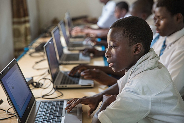 Group of Black boys in uniforms, using laptops in a classroom