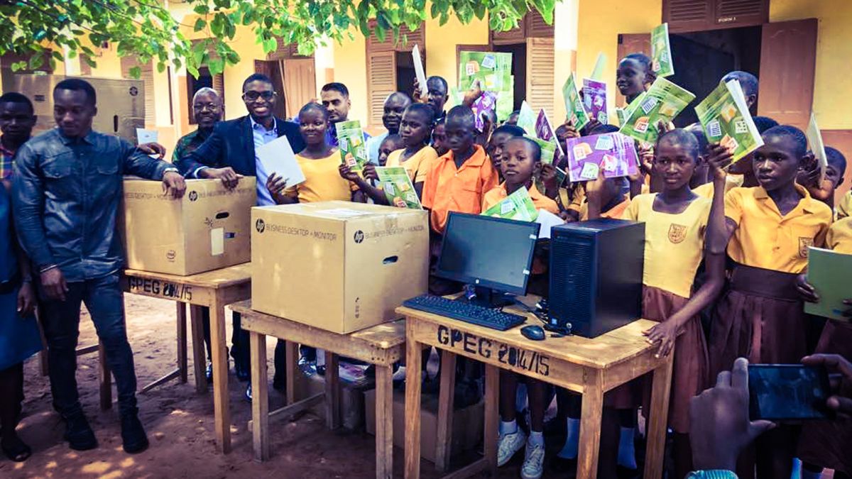 Gender-diverse group of Black children wearing school uniforms, standing with newly donated computers and textbooks